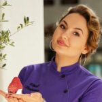 Bojana Bukvić pastry chef u ljubičastoj uniformi nagnute glave sa pojedinačnim desertom na dlanu prikazuje svoju veštinu