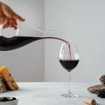 crveno vino u čaši, sa belom podlogom i pozadinom, uz čašu crvenog vina, grožđe i sireve