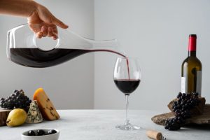 crveno vino u čaši, sa belom podlogom i pozadinom, uz čašu crvenog vina, grožđe i sireve